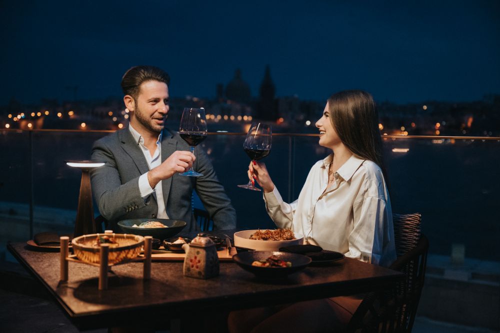 Elegant couple enjoys a candlelit dinner outdoors, clinking wine glasses.
