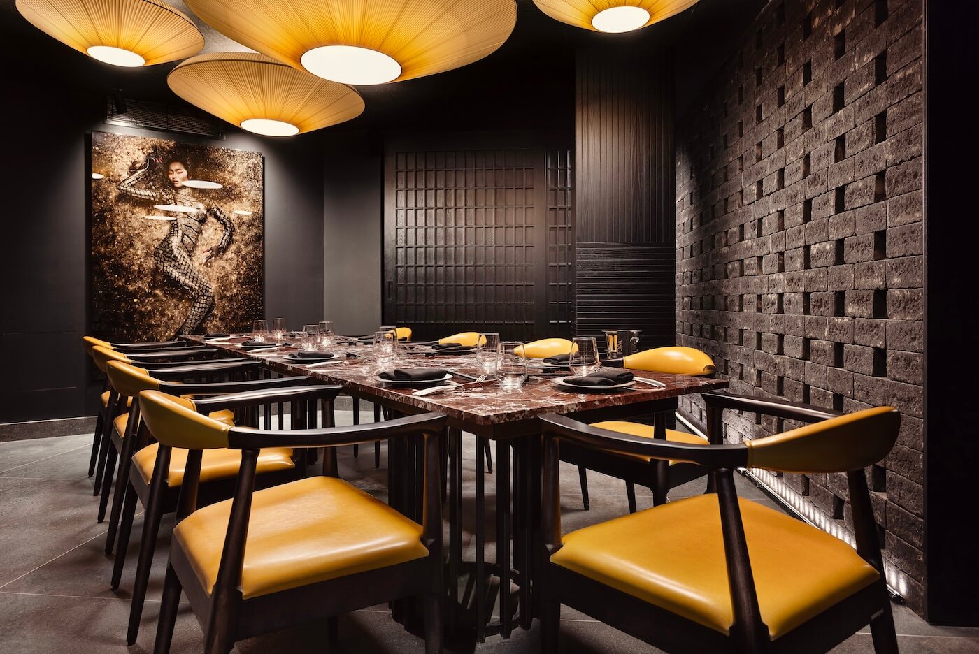 Stylish restaurant interior features elegant yellow chairs, dramatic ceiling lamps, and a glamorous woman’s wall portrait.
