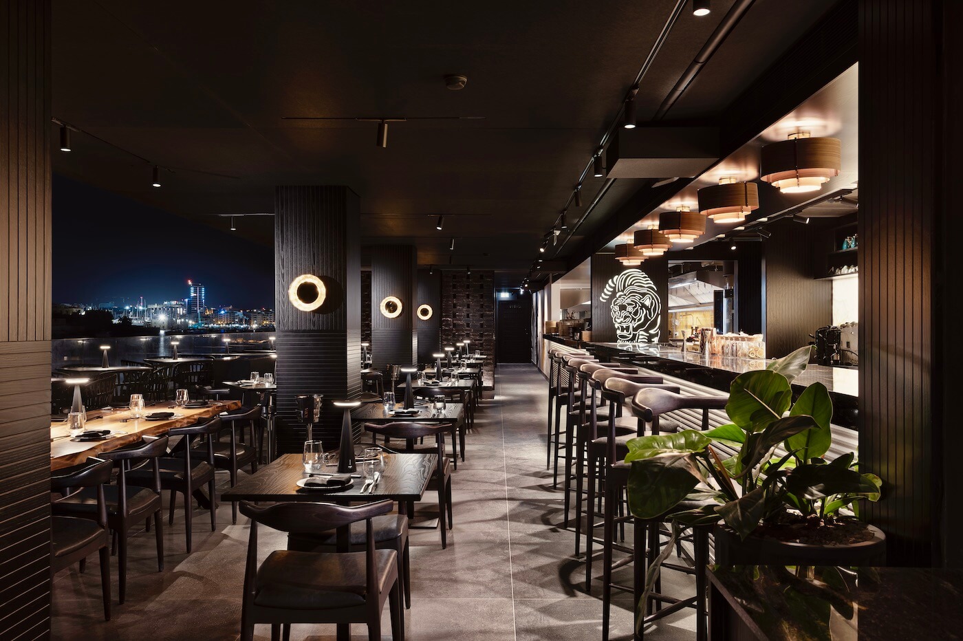 Modern restaurant interior with elegant tables, stylish lighting, city view.